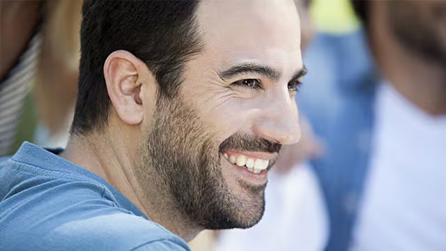 Profilbild på en ung man med skägg som ler och visar frisk munhälsa